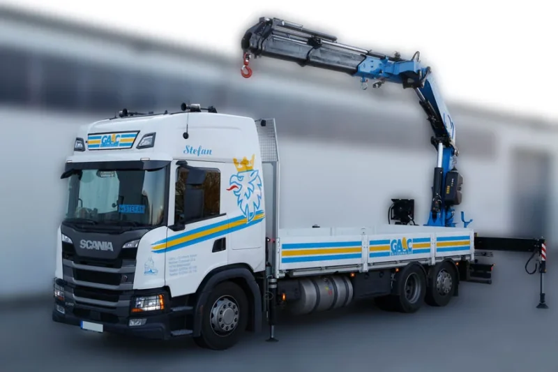 Weißer Scania Pritschenwagen von GAAC mit ausgefahrenem Ladekran am Heck